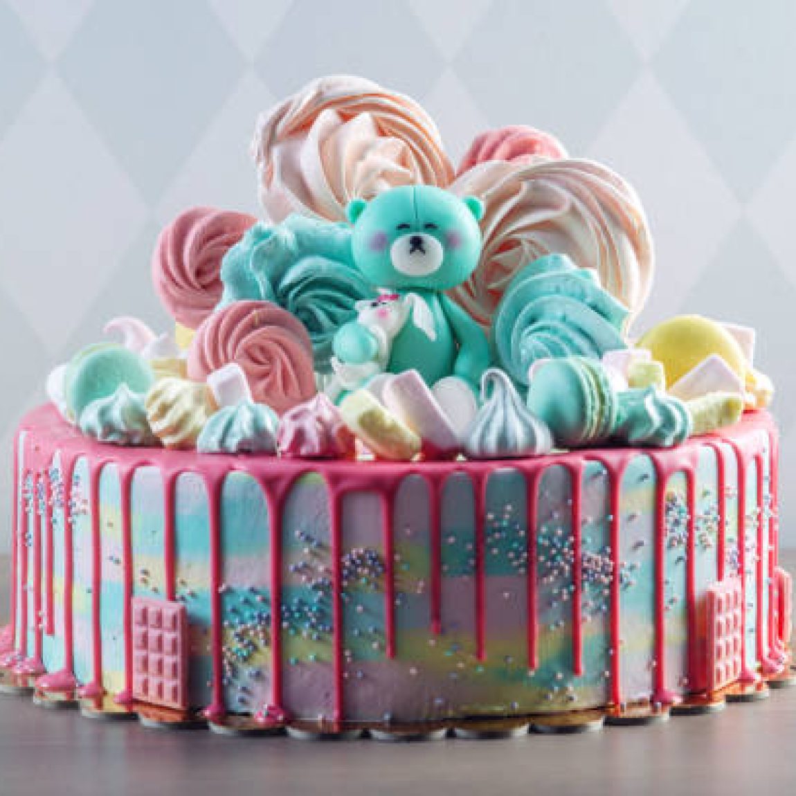 Big beautiful kids cake decorated with turquoise Teddy bear and colorful meringues and marshmallows. The concept of festive desserts for the birthday children